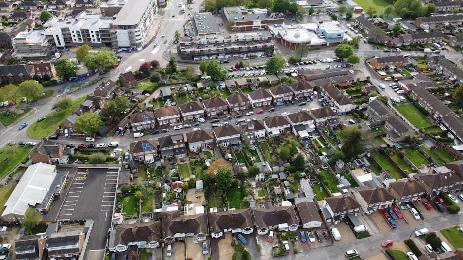 An aerial view of a suburban residential area showing a variety of gardens with well-maintained lawns, flowerbeds, and hedges. The image features row houses with small backyard gardens, some with pave